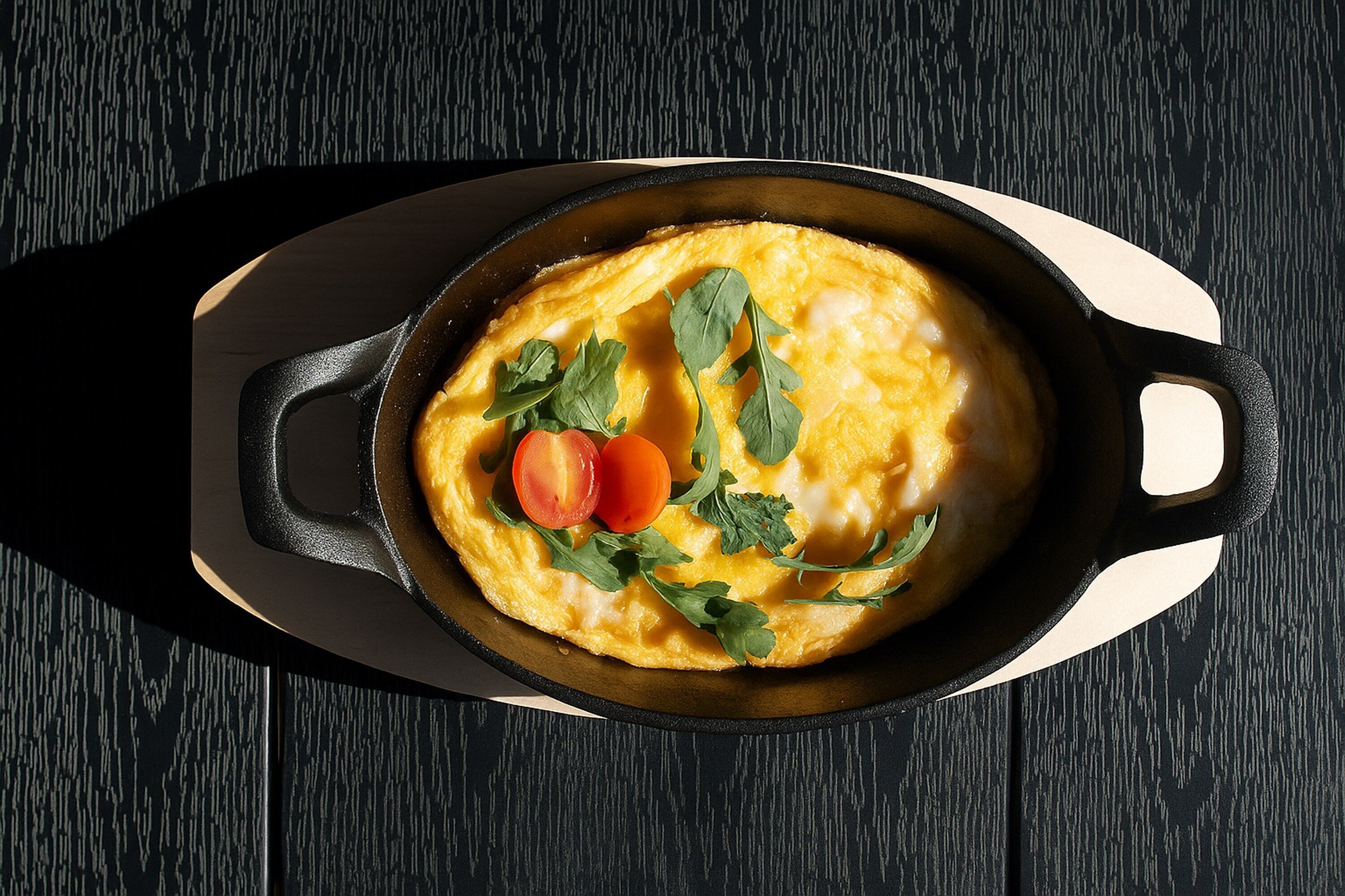 Una sartén con una tortilla adornada con hierbas y tomates sobre una tabla de madera.
