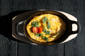 A skillet with an omelette garnished with herbs and tomatoes on a wooden board. - Boutique Hotel Echo Residence (Belgrade)