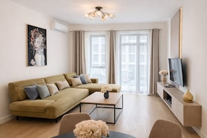 A modern living room with a sectional sofa, a coffee table, a flat-screen TV, and a large window with curtains. - Boutique Hotel Echo Residence (Belgrade)