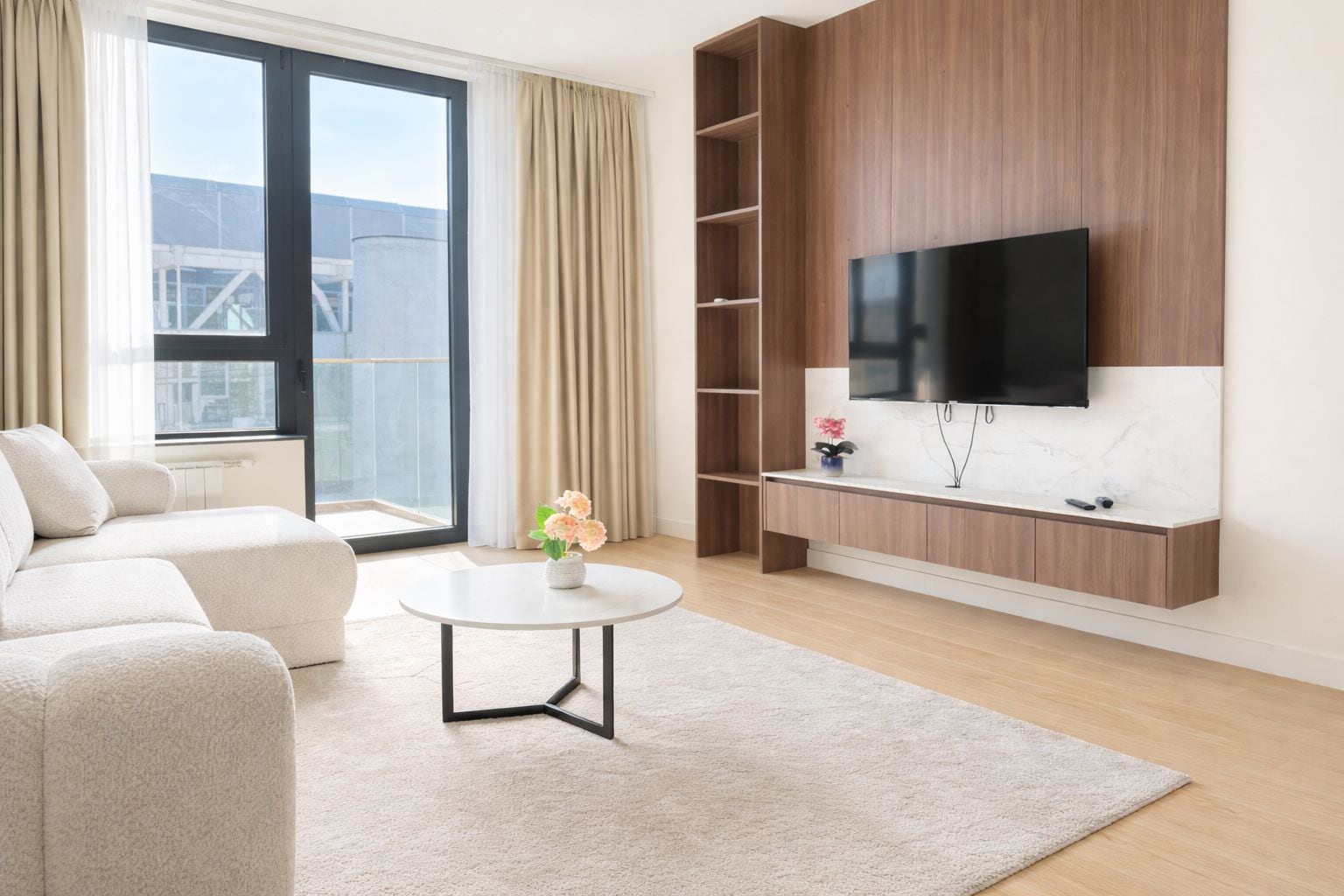A modern living room with a sofa, a coffee table, a TV mounted on a wooden wall, and a view of the city through large windows.