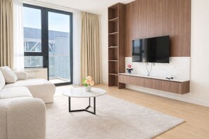 A modern living room with a sofa, a coffee table, a TV mounted on a wooden wall, and a view of the city through large windows. - Boutique Hotel Echo Residence (Belgrade)