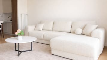 Una sala de estar con un sofá blanco, una mesa redonda de centro y un jarrón con flores.