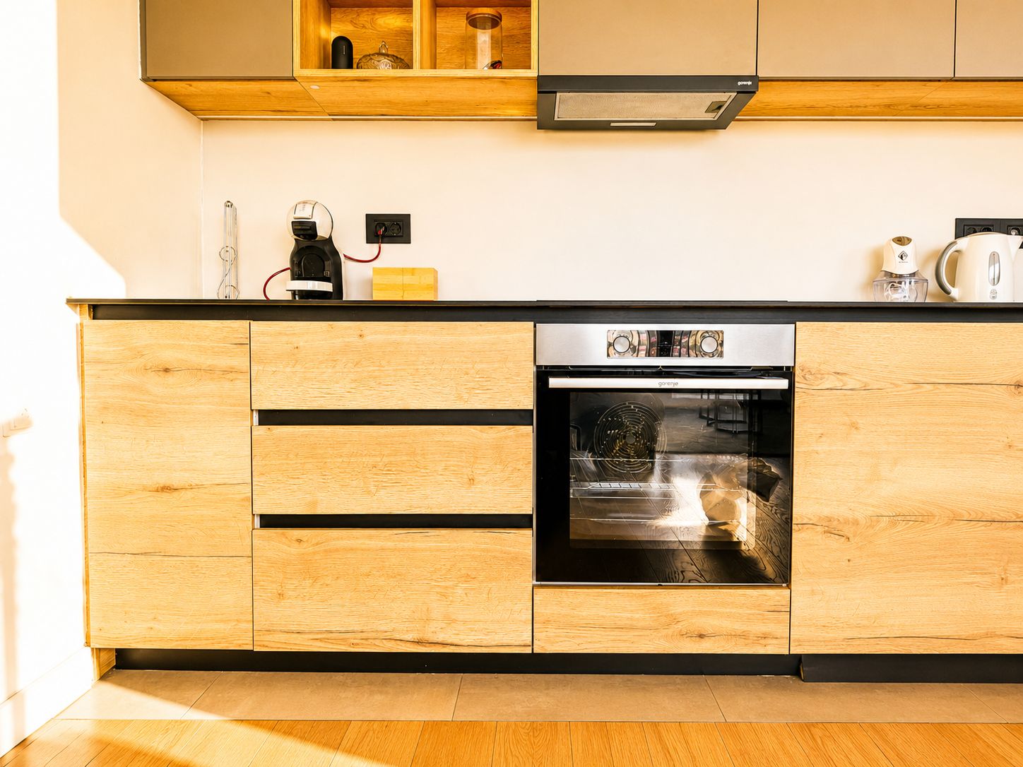 A modern kitchen with wooden cabinetry, a built-in oven, and a coffee maker on the countertop.