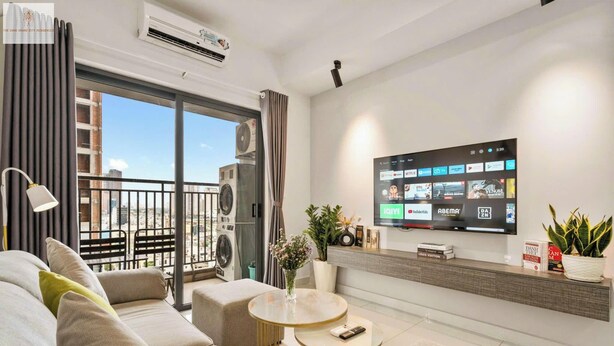 Un salon moderne doté d’un grand téléviseur à écran plat fixé au mur, d’un canapé, d’une petite table ronde et d’un balcon offrant une vue sur la ville.