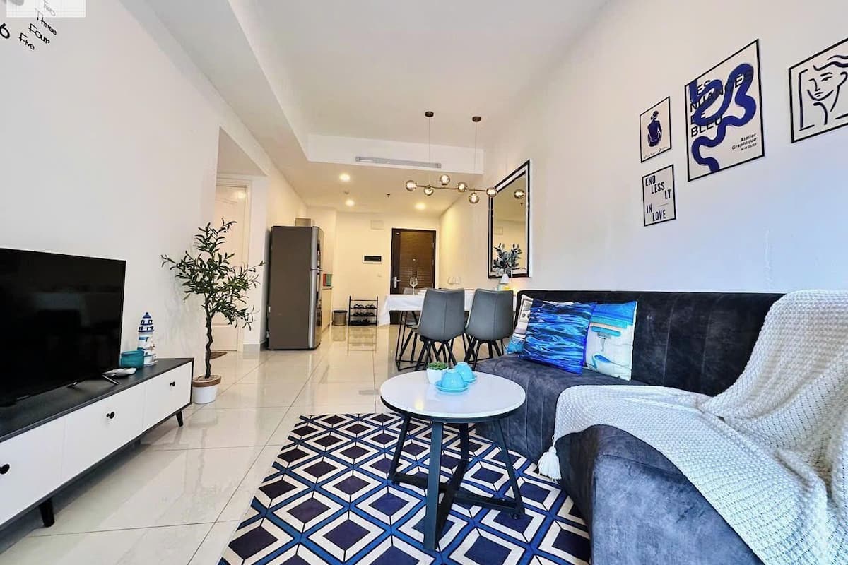 A modern living room with a flat-screen TV, a grey sofa, a patterned rug, and a dining area with chairs and a table.