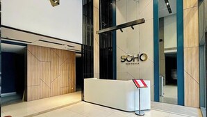 Un espace d’accueil moderne comprenant un comptoir de réception, un mur recouvert de panneaux en bois et une enseigne indiquant « SOHO RESIDENCE ».