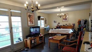 Een gezellige woonkamer met een televisie, houten meubels, een eettafel en uitzicht door grote ramen.