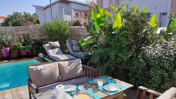 Een houten terras met een zwembad, ligbedden en een eettafel.