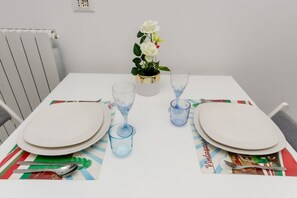 Une table à manger dressée avec de l’assiette blanche, des verres bleus et une petite rose blanche dans un vase doré.