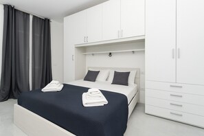 Une chambre à coucher moderne avec un lit, une armoire blanche et des rideaux gris.
