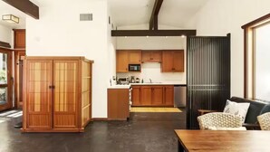 Ampla sala de estar com armário de madeira, cozinha com armários de madeira, sofá preto e mesa de jantar.