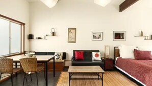 Uma sala de estar moderna com um sofá, uma mesa de jantar e cadeiras. Há obras de arte nas paredes e uma cama com um cobertor vermelho.