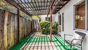 Área de varanda coberta com cerca de madeira, um banco e piso verde.