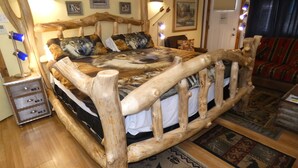 Een rustiek houten bed met een uniek ontwerp, een nachtkastje met lades, en een kamerbreed vloerkleed.