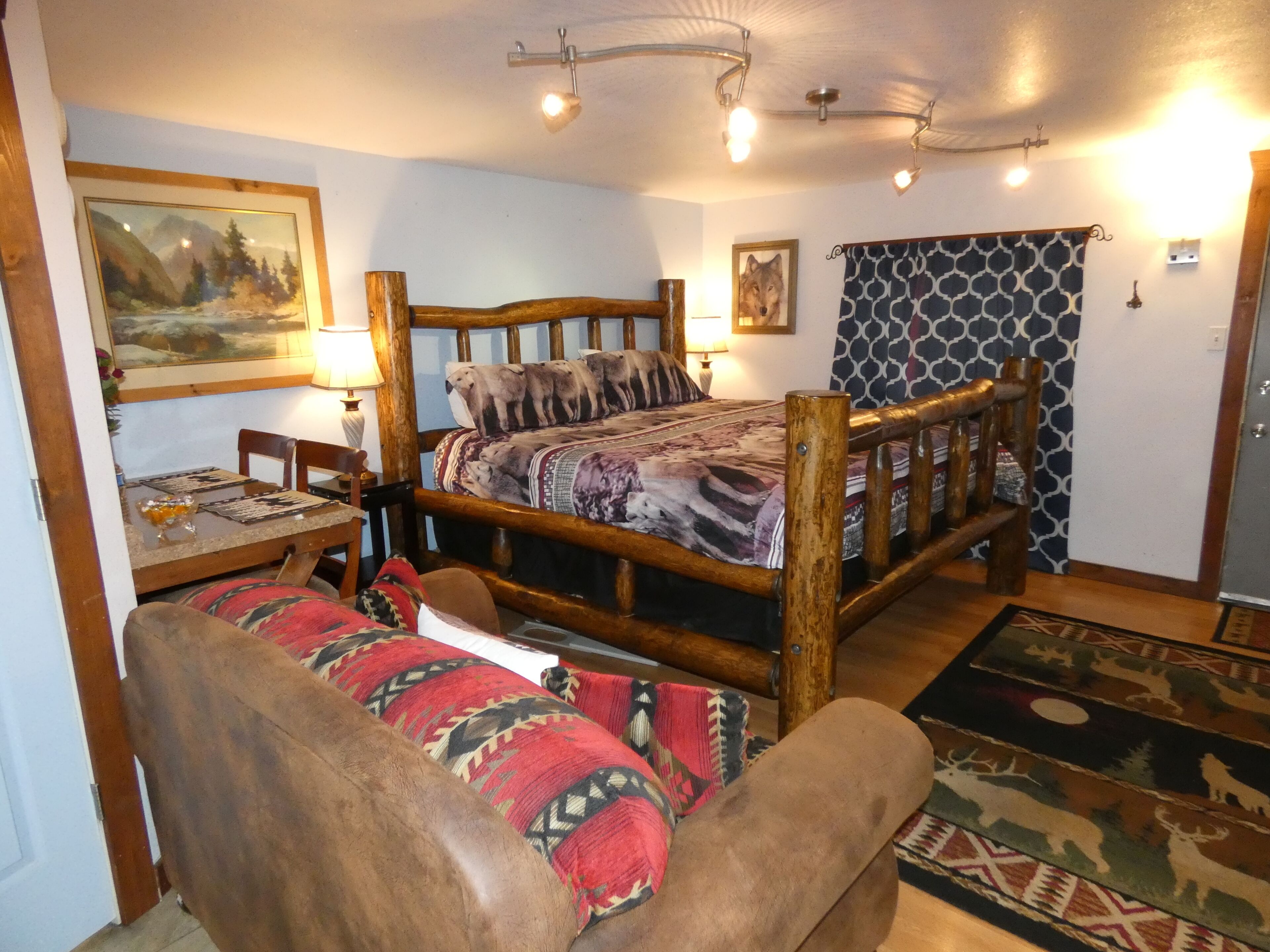 Una habitación con una cama de madera, una mesa de comedor, una silla, un tapete y un cuadro en la pared.