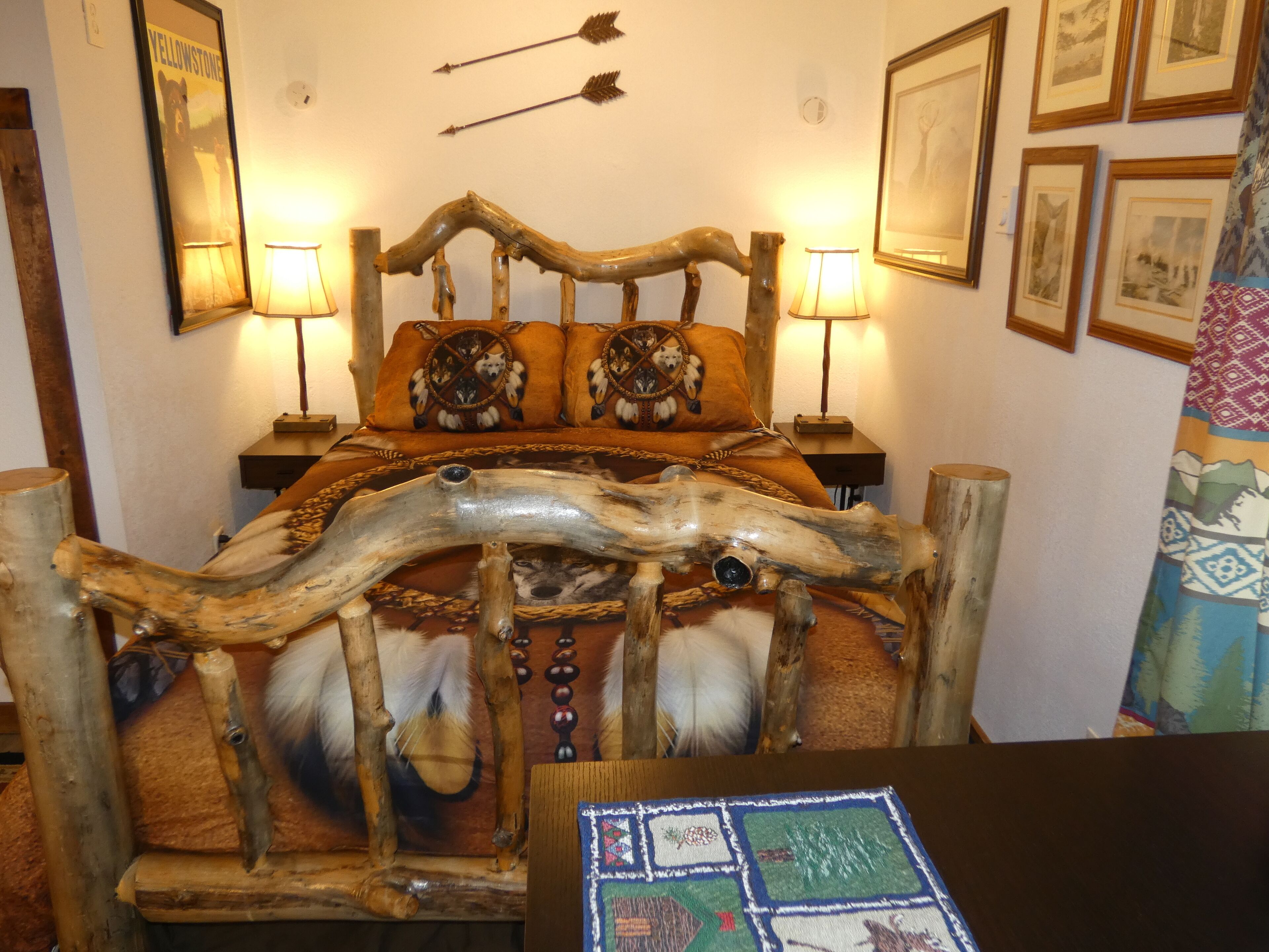 Una cama con cabecera de madera, dos almohadas con motivos de animales y una manta estampada con un diseño de pelo. Hay dos lámparas de noche y un cuadro en la pared.