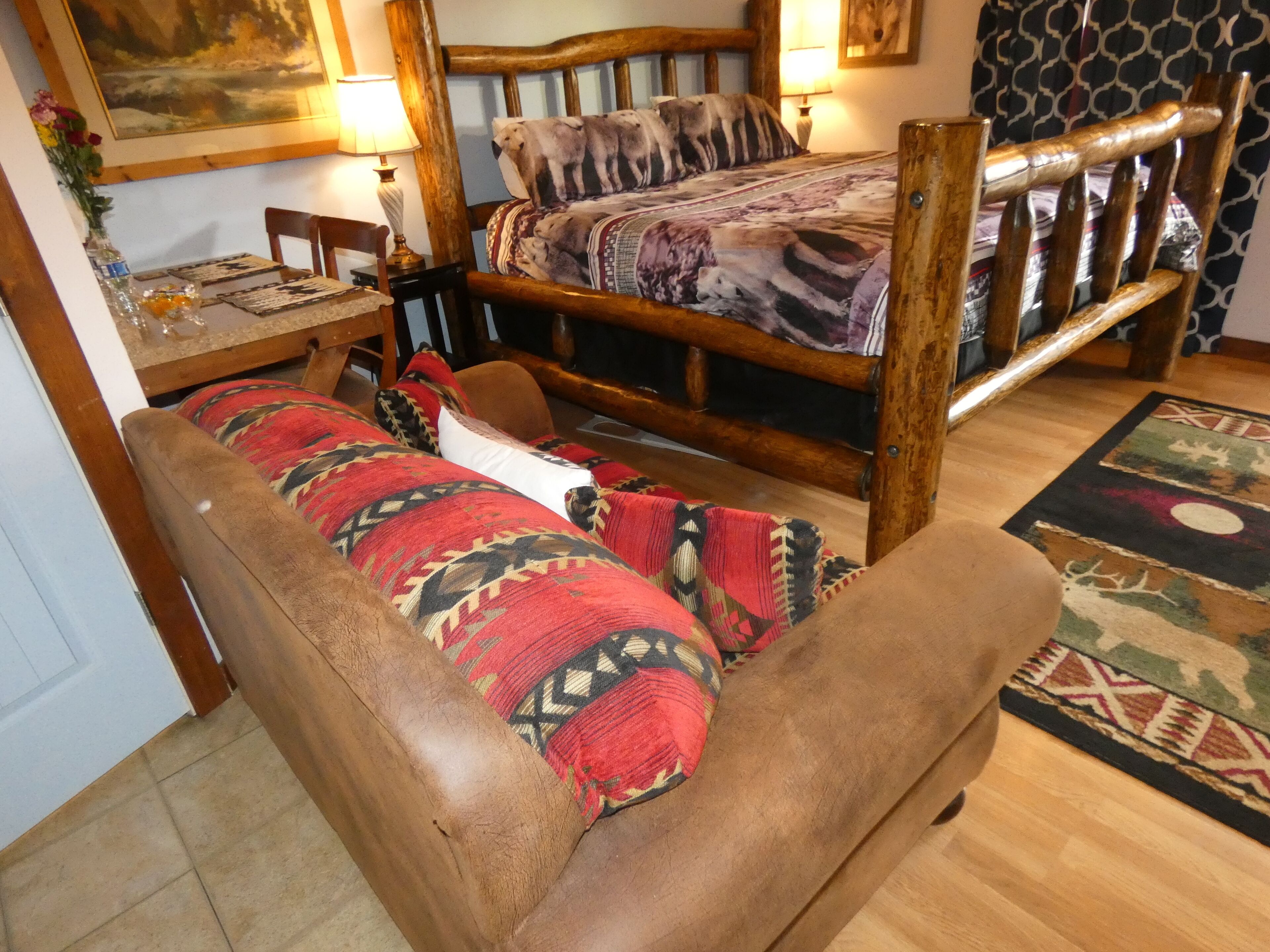 Une pièce chaleureuse avec un lit en bois, un canapé, une petite table avec une lampe et un tableau accroché au mur.