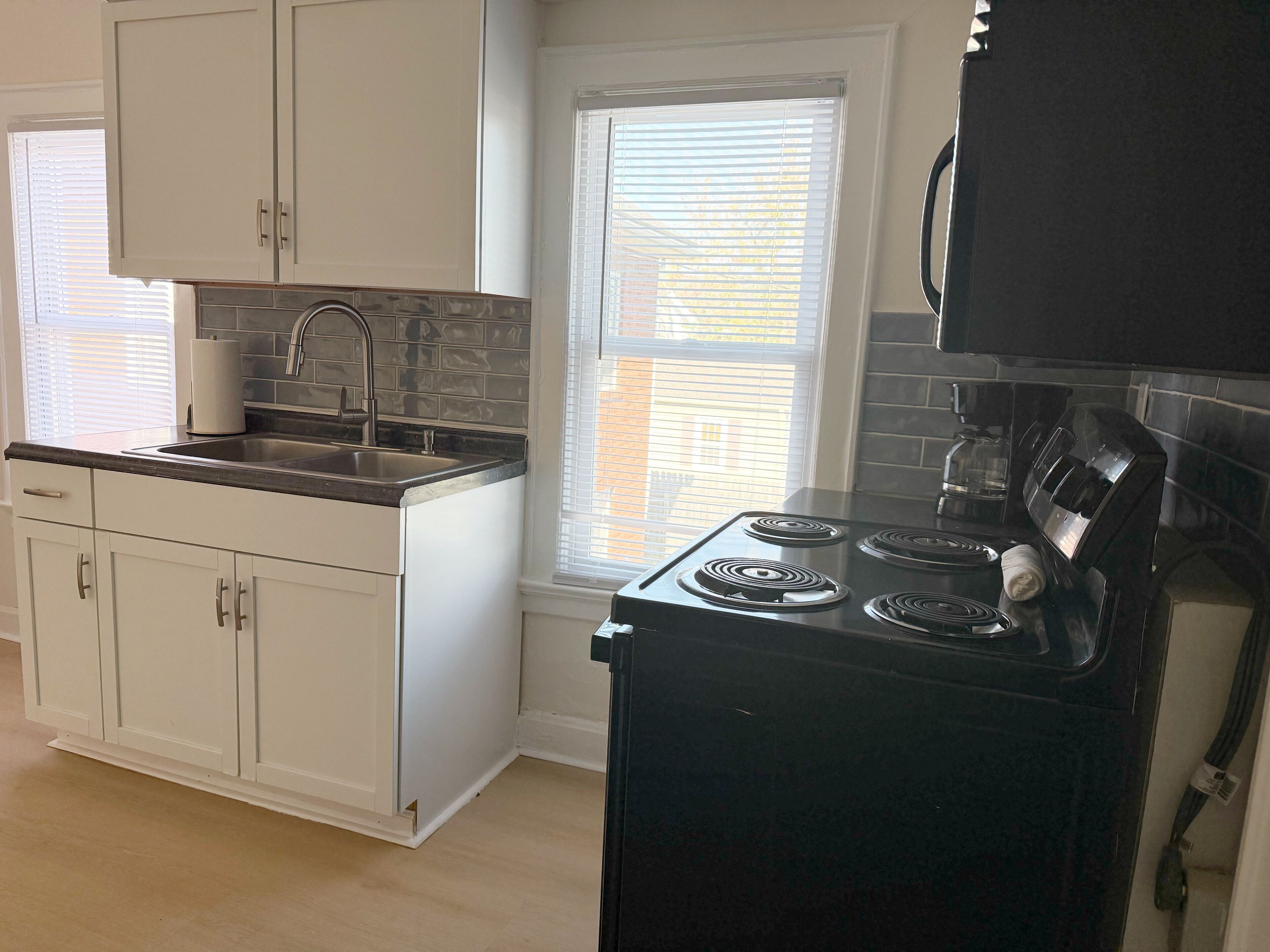 A kitchen with white cabinets, a black stove, and a window with blinds.
