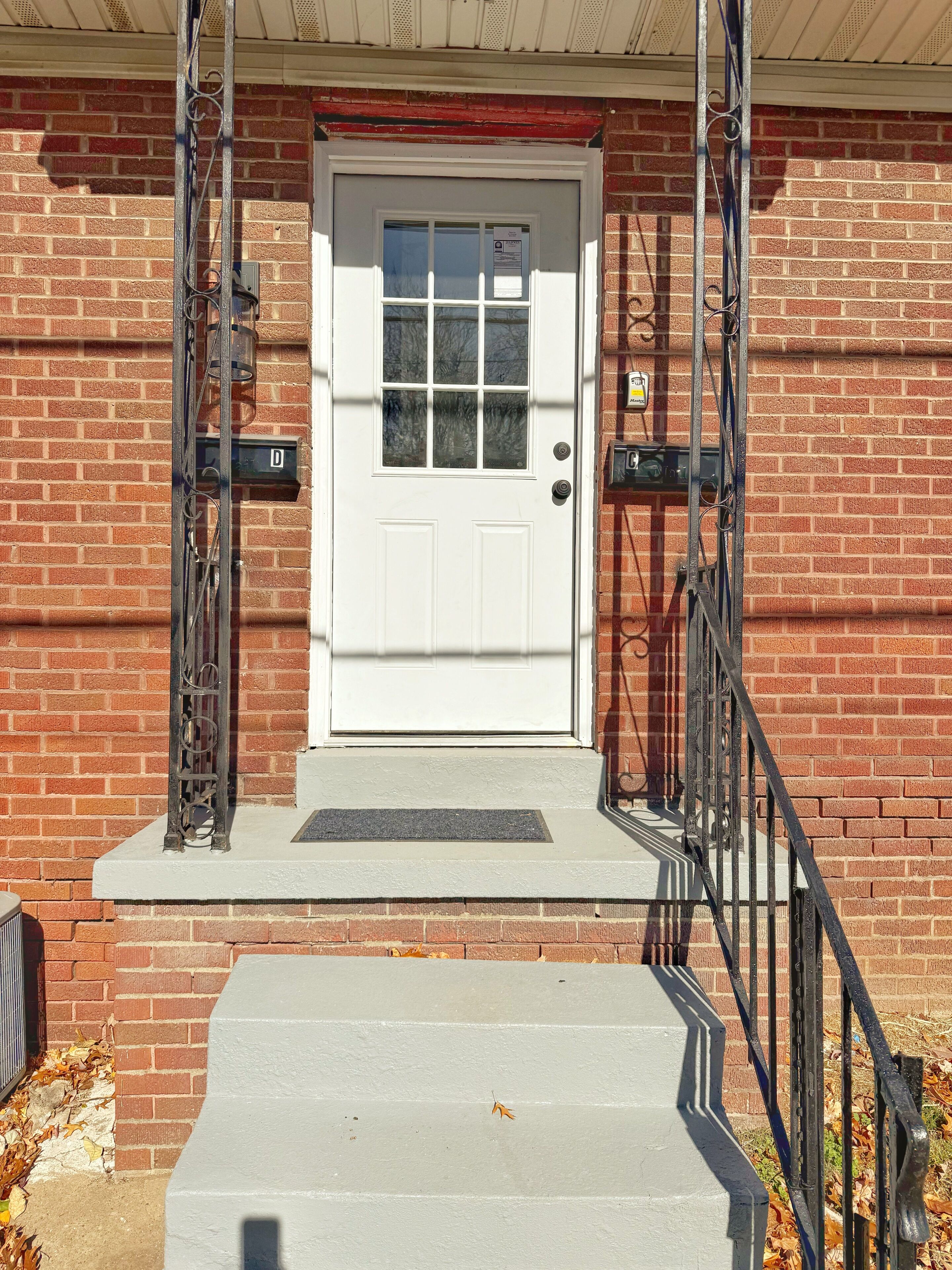 A white door with a small window, a metal staircase, and a brick wall.