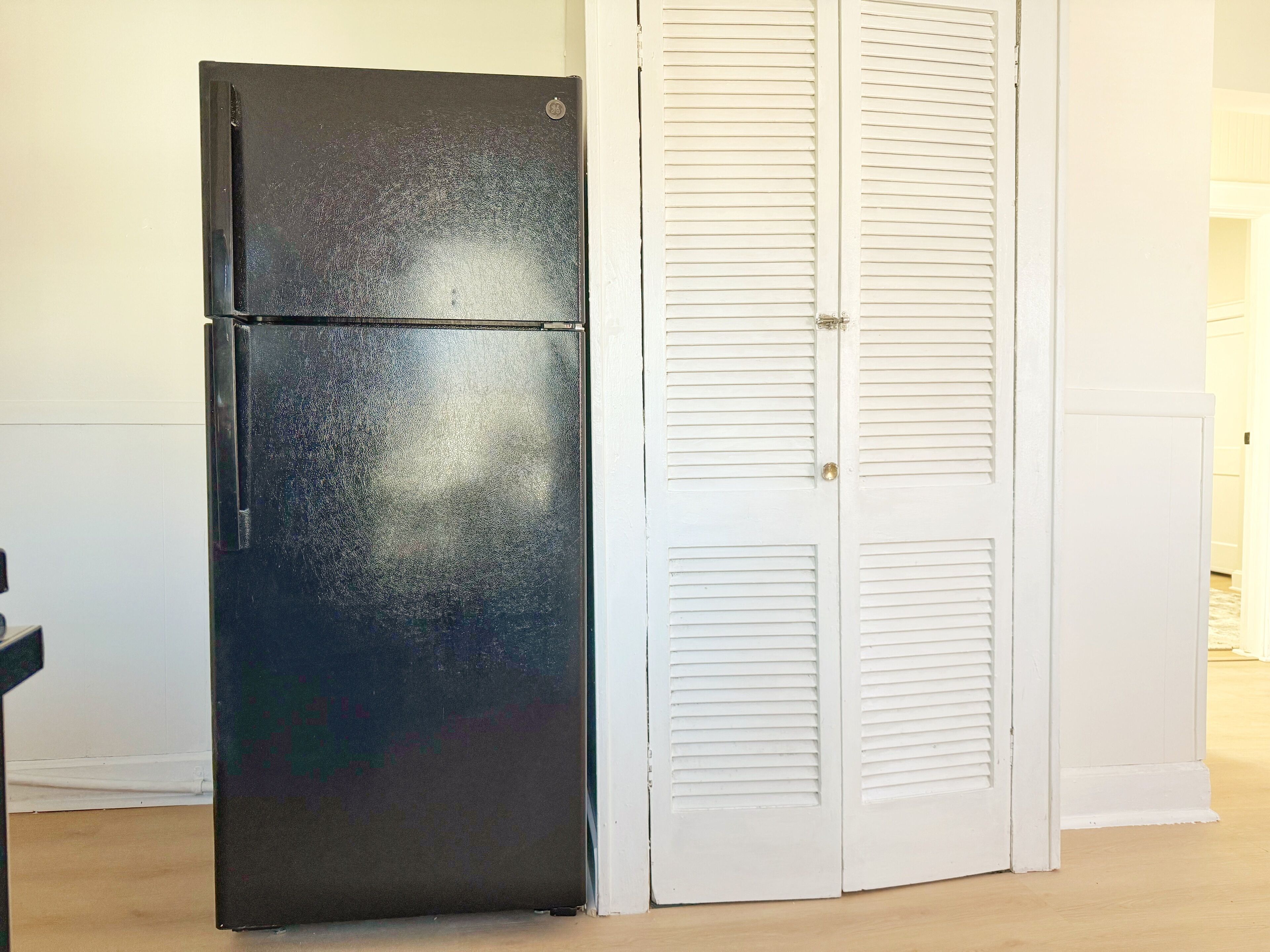 Ein schwarzer Kühlschrank neben einer weißen Tür mit Lamellen.