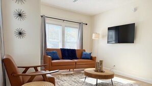 Een woonkamer met een bruine leren bank, twee fauteuils, een salontafel en een vloerkleed.