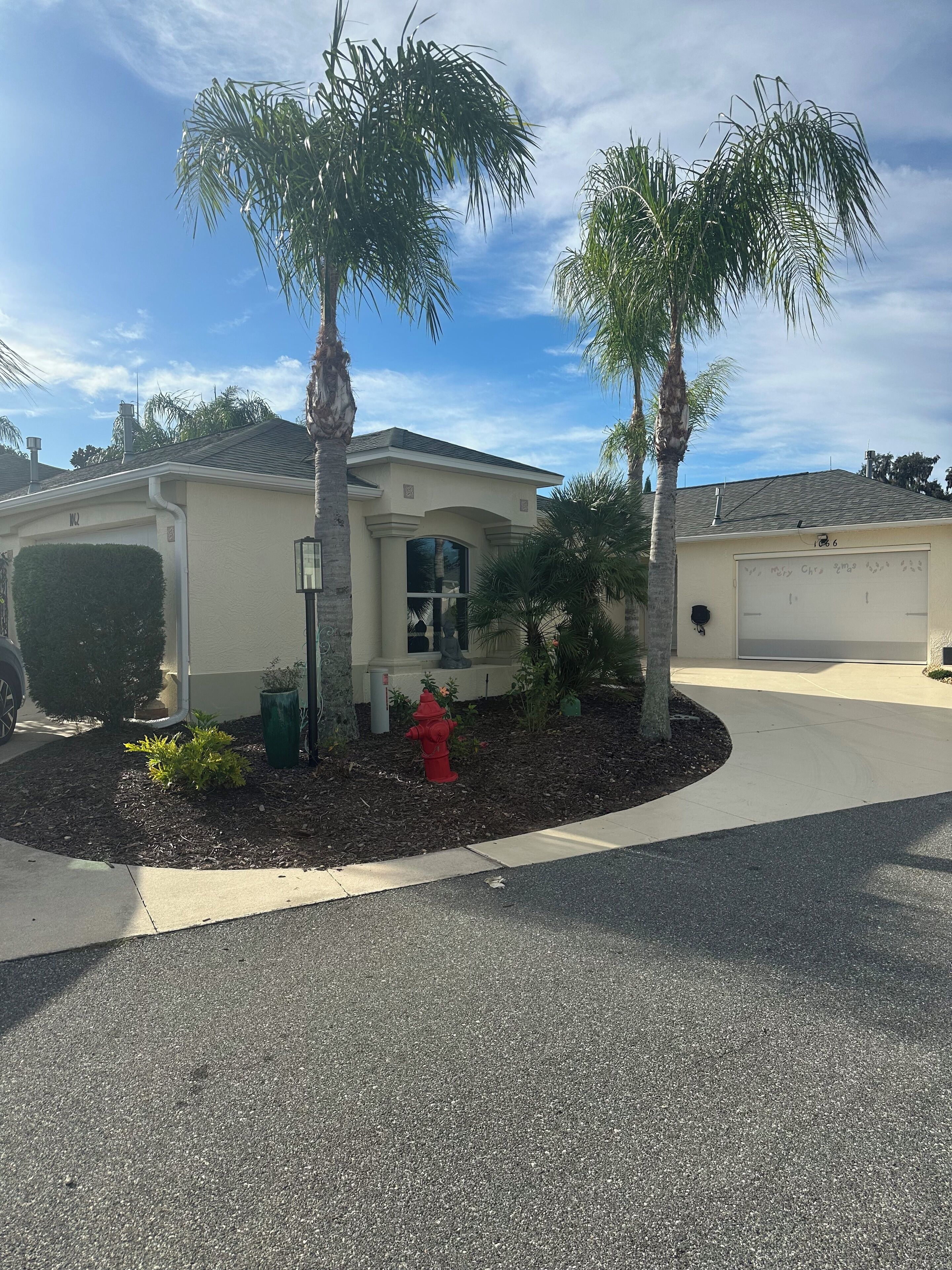 A single-story house with a garage, surrounded by a landscaped garden with palm trees and a red fire hydrant.
