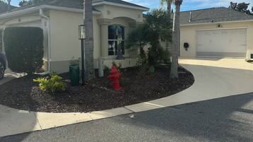 A single-story house with a garage, surrounded by a landscaped garden with palm trees and a red fire hydrant.