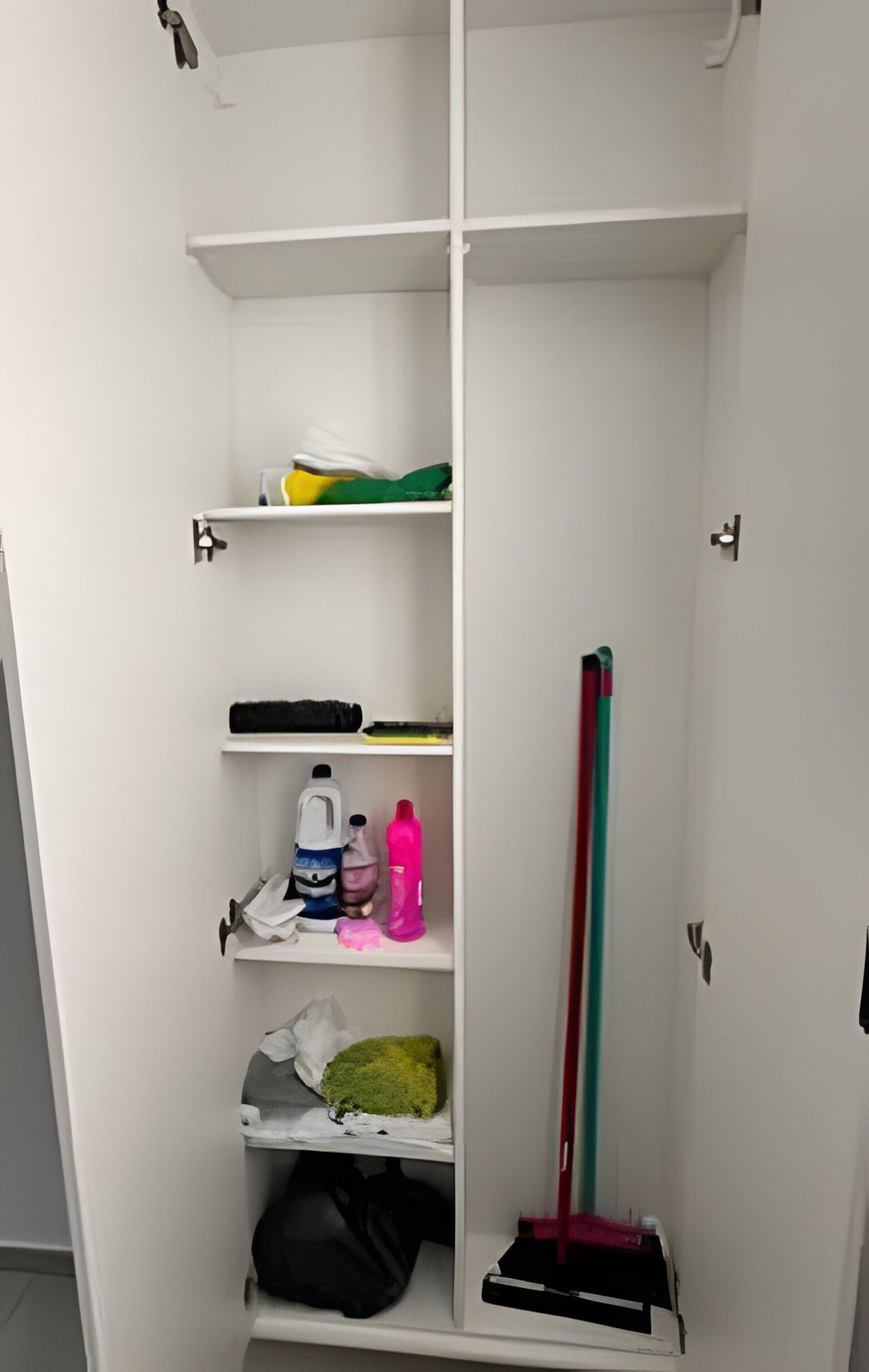 Un armario blanco con varios estantes, una barra para colgar ropa y una escoba apoyada en la pared.