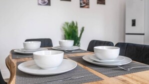 Una mesa de comedor con cuatro cuencos y platos blancos, una planta al fondo y un refrigerador a la derecha.