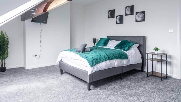 Un dormitorio con una cama, una mesita de noche, una planta en maceta y un estante en la pared.