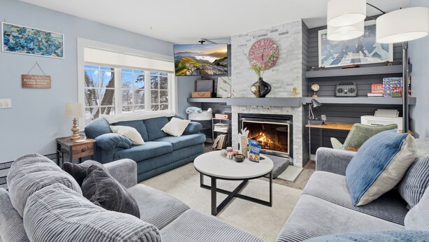 Ein Wohnzimmer mit Kamin, blauen Sofas und einem Fernseher.