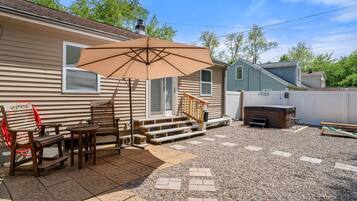 A backyard with a patio, wooden furniture, a barbecue grill, and a covered seating area.