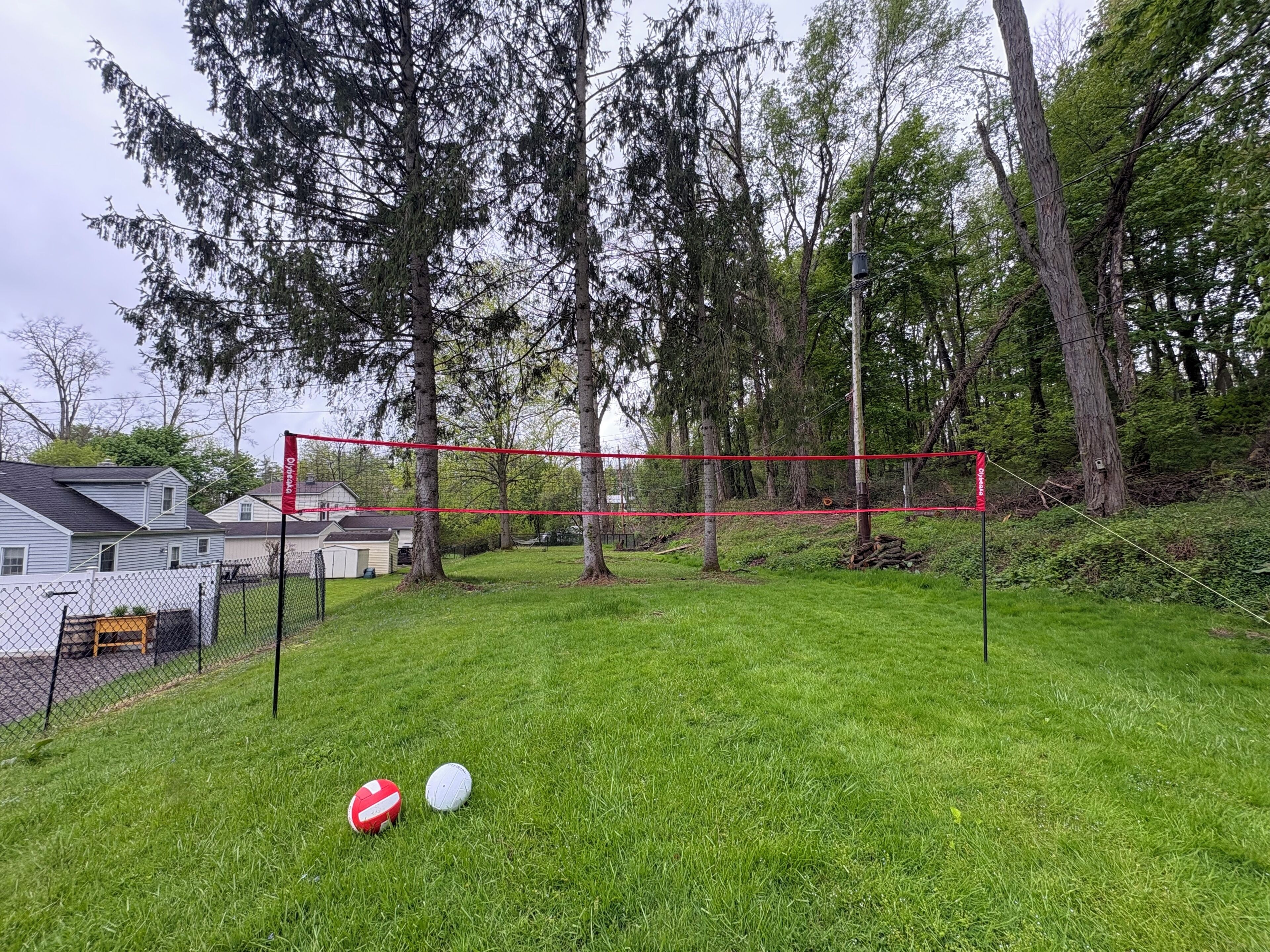 A fenced outdoor area with a volleyball net, two volleyballs, and a red banner.