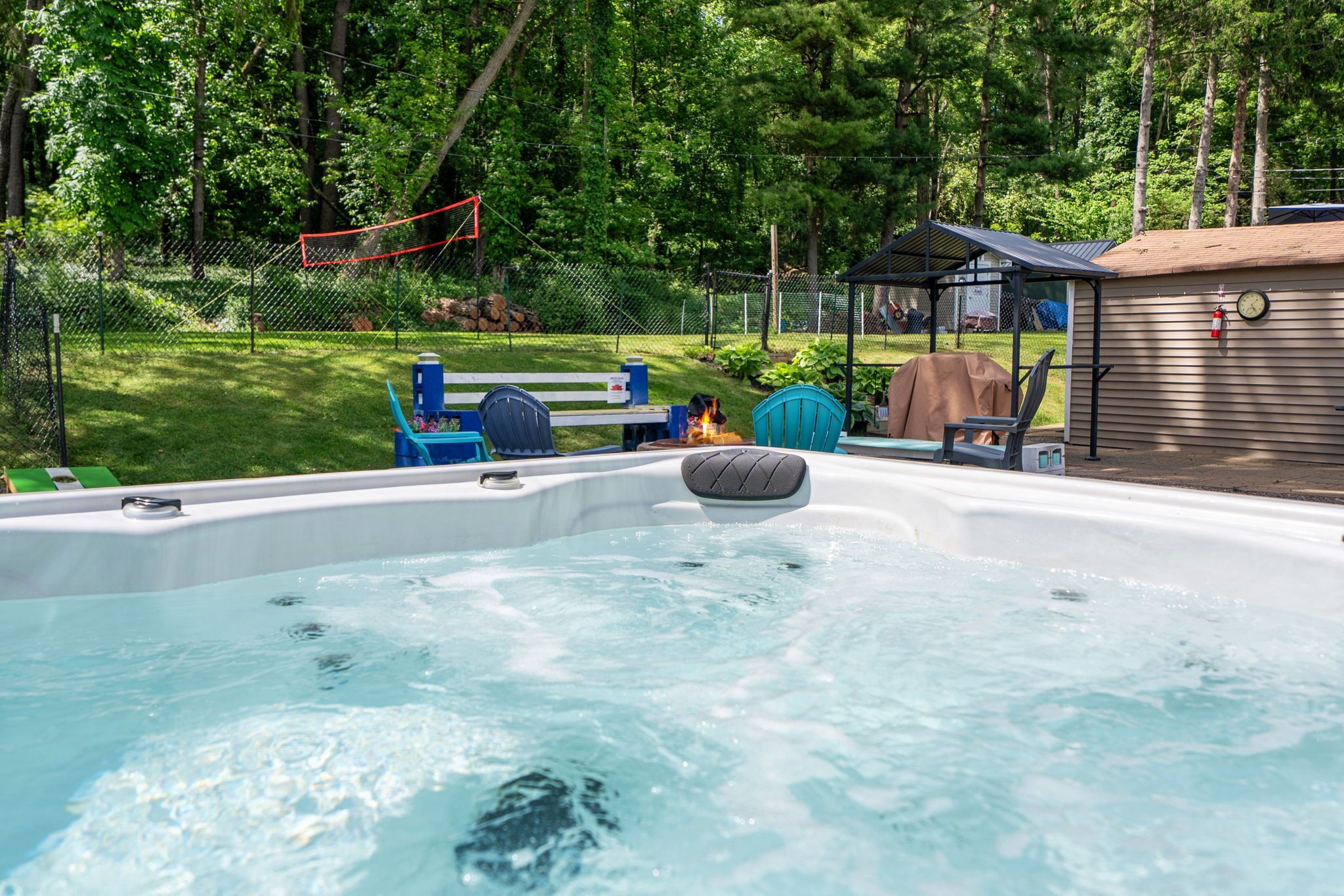 Un jacuzzi con chimenea, rodeado por un patio cercado con un banco y un área de estar cubierta.