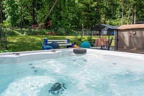 Un jacuzzi con chimenea, rodeado por un patio cercado con un banco y un área de estar cubierta.
