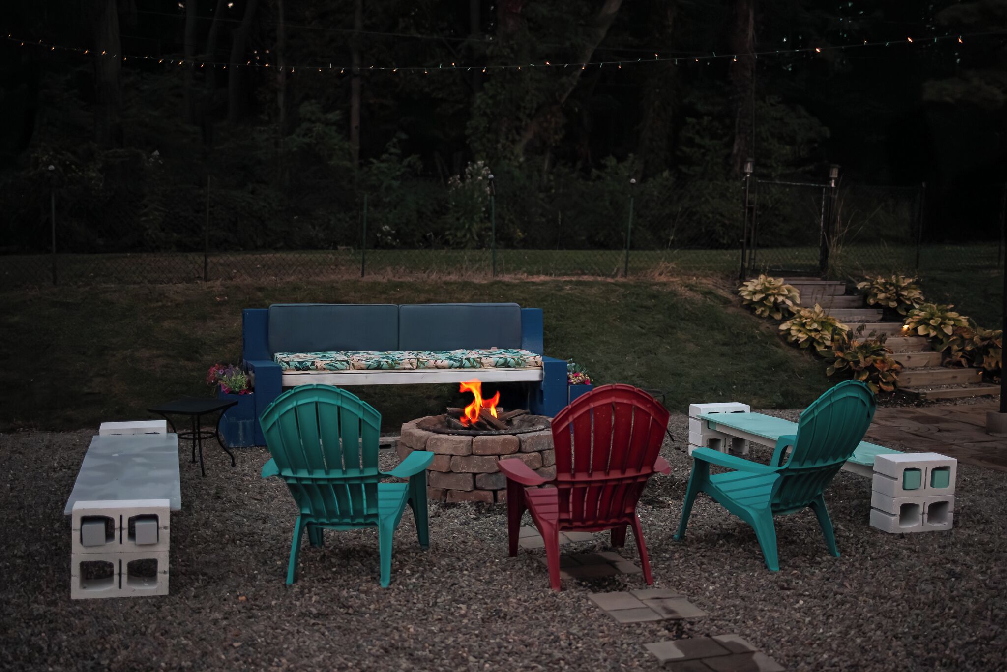 A fire pit with chairs and a bench in a garden setting.