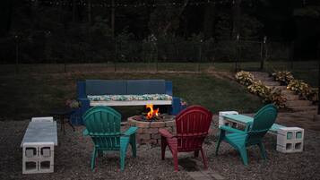A fire pit with chairs and a bench in a garden setting.