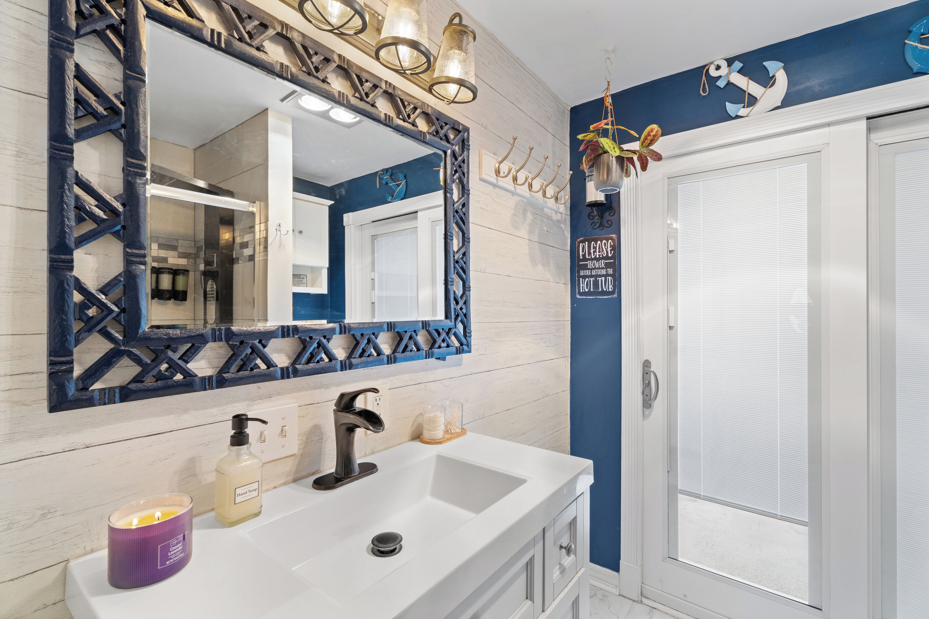 Un baño con lavamanos blanco, un espejo grande y una pared azul decorativa.