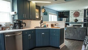 Eine moderne Küche mit dunkelblauen Schränken, einem Geschirrspüler, einer Kaffeemaschine und einer Wanduhr.