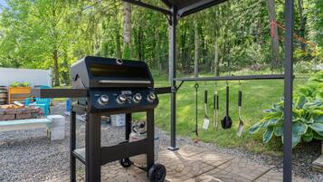A barbecue grill under a covered patio with a grassy area and trees in the background.