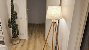 Une pièce avec un plancher en bois, un lampadaire, un cactus et un lit avec des serviettes.