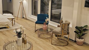 Un salon moderne avec un plancher en bois, un fauteuil bleu, une table basse ronde en verre et une petite table d’appoint avec une lampe.