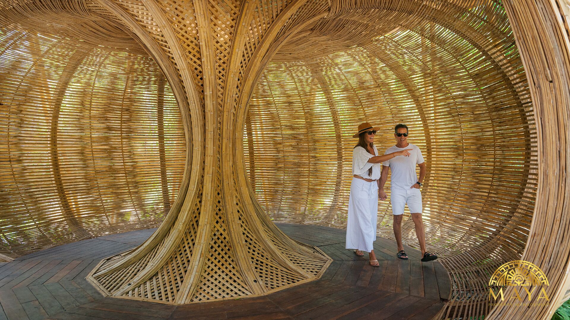A couple standing in a circular, woven structure with a wooden floor.