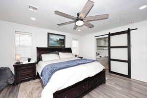 Ein Schlafzimmer mit einem großen Bett, einem Deckenventilator, einem Gemälde, einer Schiebetür und einem kleinen Nachttisch mit Lampe.