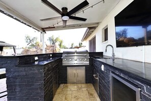 Eine Außenküche mit Gasgrill, integriertem Spülbecken und Deckenventilator.