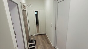 Kapea käytävä, jonka seinät ovat valkoiset ja lattia puuta. Oikealla puolella on kaksi ovea ja vasemmalla puolella peilillä varustettu vaatekaappi.