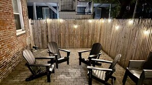 En uteplats med fyra Adirondack-stolar placerade runt ett tegelbelagt område, omgiven av ett bambustaket och en tegelmur.