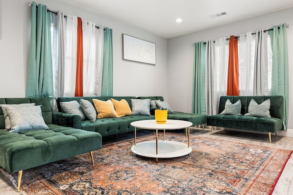Una sala de estar moderna con dos sofás verdes, una mesa de centro redonda y una alfombra estampada.