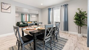 Un coin repas avec une table dressée pour quatre personnes, un canapé vert en arrière-plan et une plante en pot près de la fenêtre.