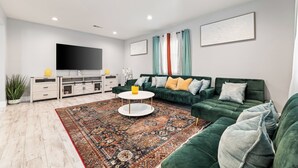 Un salon moderne avec un canapé vert, une table basse ronde et un téléviseur à écran plat fixé au mur.